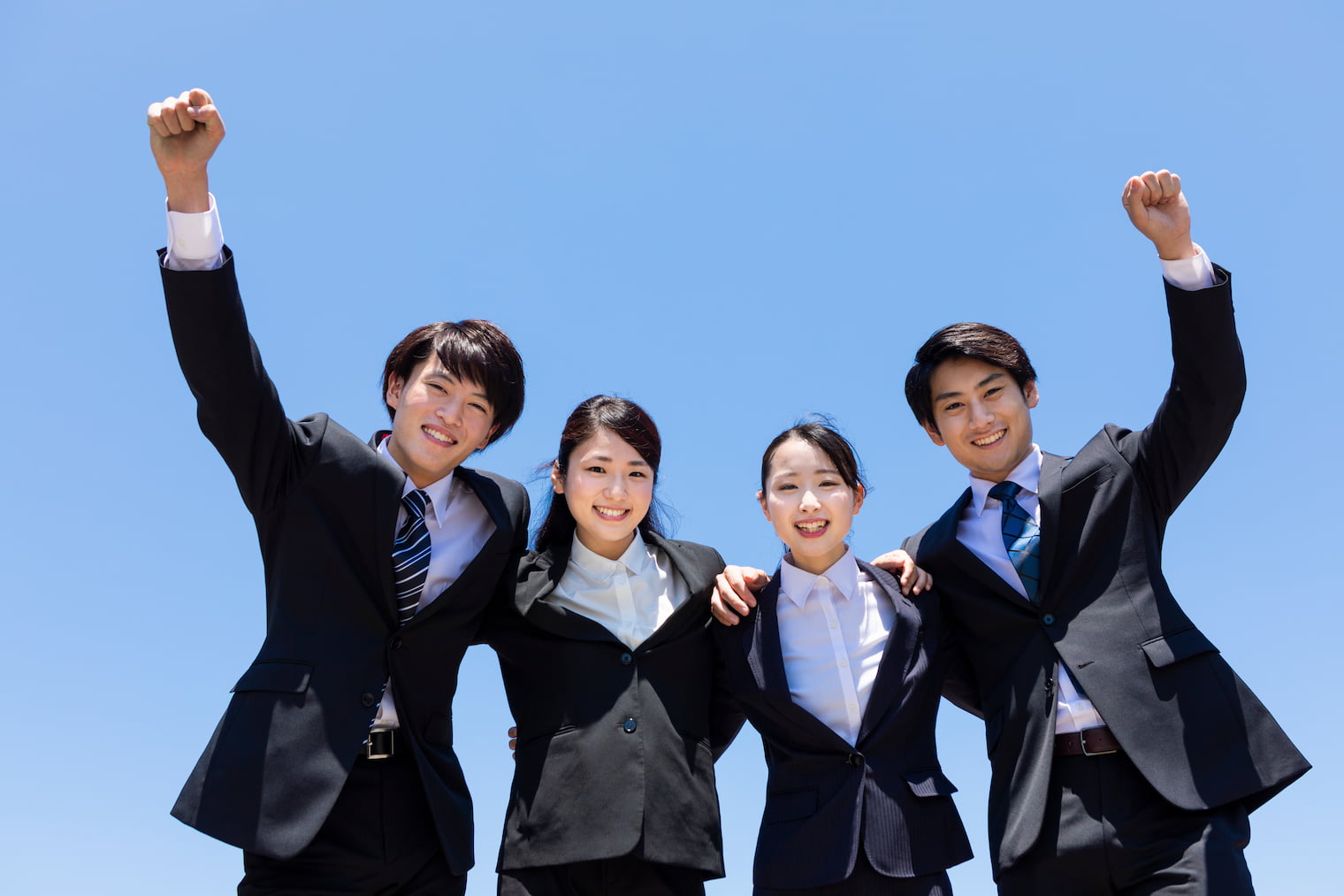 肩を組んで空に向かってこぶしを突き上げている新社会人
